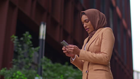 muslim businesswoman wearing hijab standing outside modern office getting good news about job offer or promotion on mobile phone 2