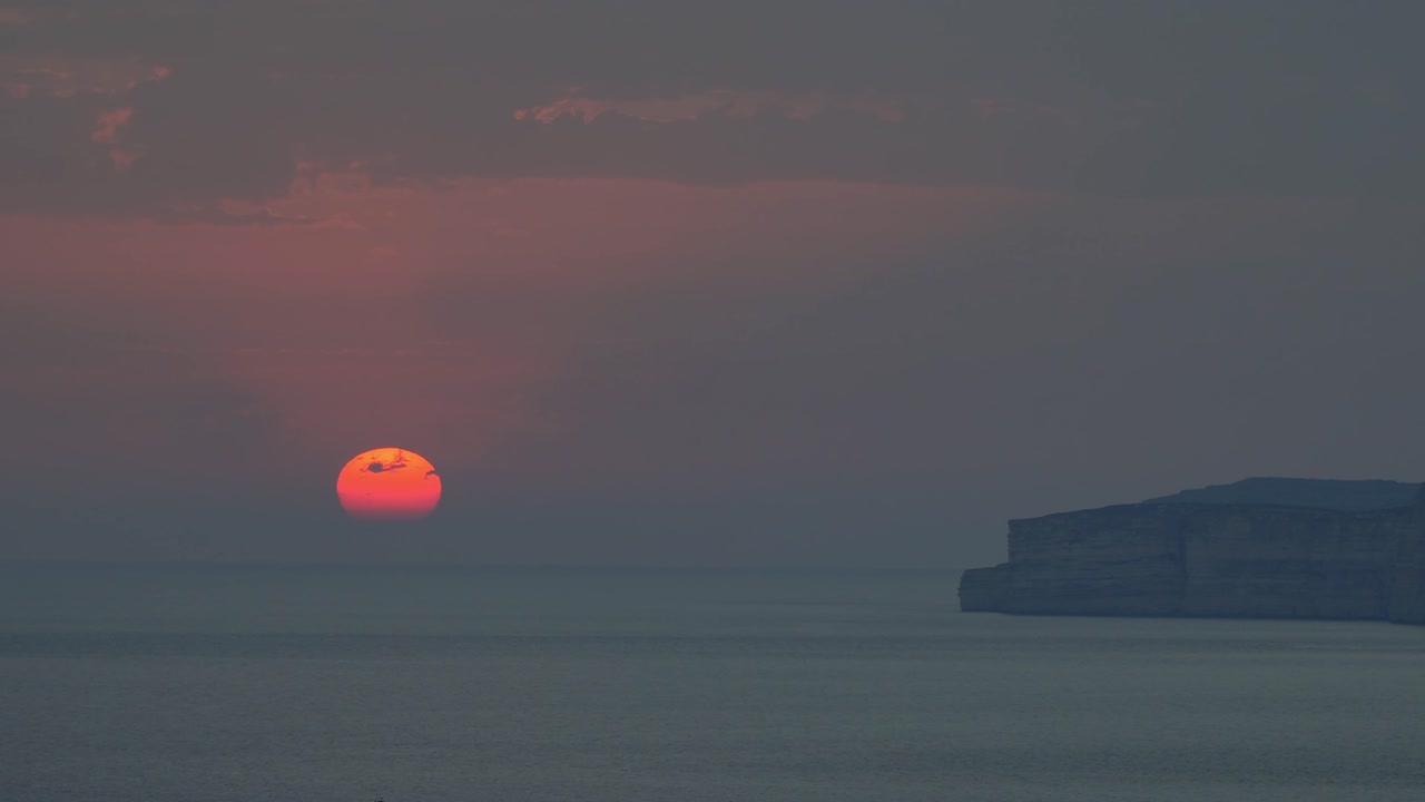Beautiful sunset as the orange sun begins to disappear behind the horizon over the Mediterranean Sea with the rocky coast of Gozo aside in Malta.