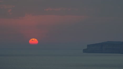 beautiful sunset as the orange sun begins to disappear behind the horizon over the mediterranean sea with the rocky coast of gozo aside in malta.