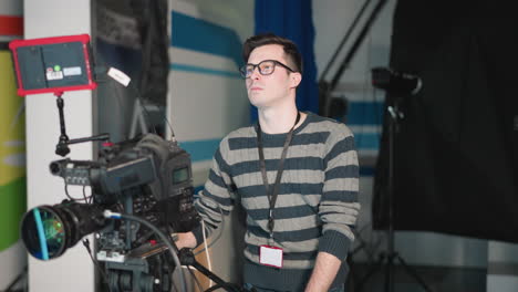 close-up of camera operator adjusting broadcast camera with attached monitor in studio. filming equipment and crew setup in modern tv production space