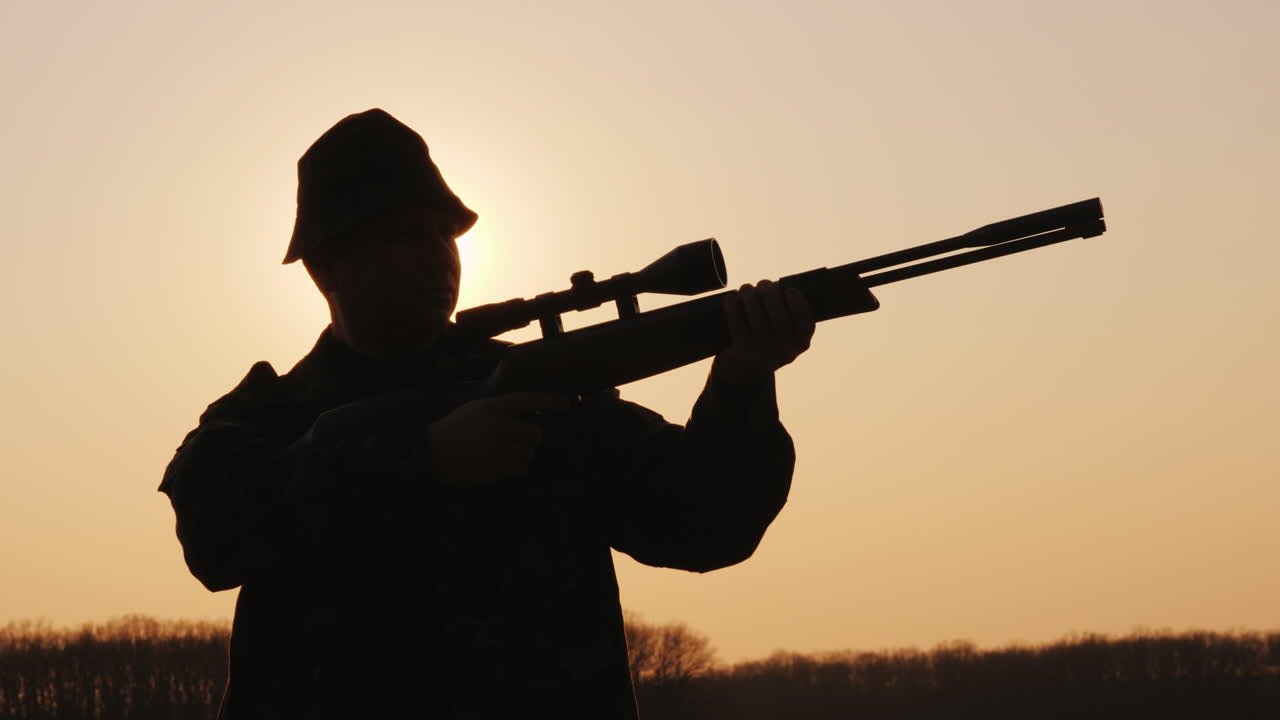 силуэт охотника с ружьем, солнечные лучи светят ему в лицо