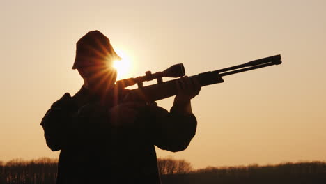 silhouette of a hunter with a gun the sun's rays shine in his face