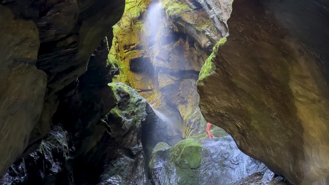 เด็กผู้หญิงคนหนึ่งเดินออกมาบนชานหินภายใน Wilsons Creek Chasm, Haast Pass, นิวซีแลนด์ หน้าผาสูงตระหง่านและน้ำที่ไหลเชี่ยวล้อมรอบหุบเขาลึกที่สวยงามและน่าทึ่งแห่งนี้