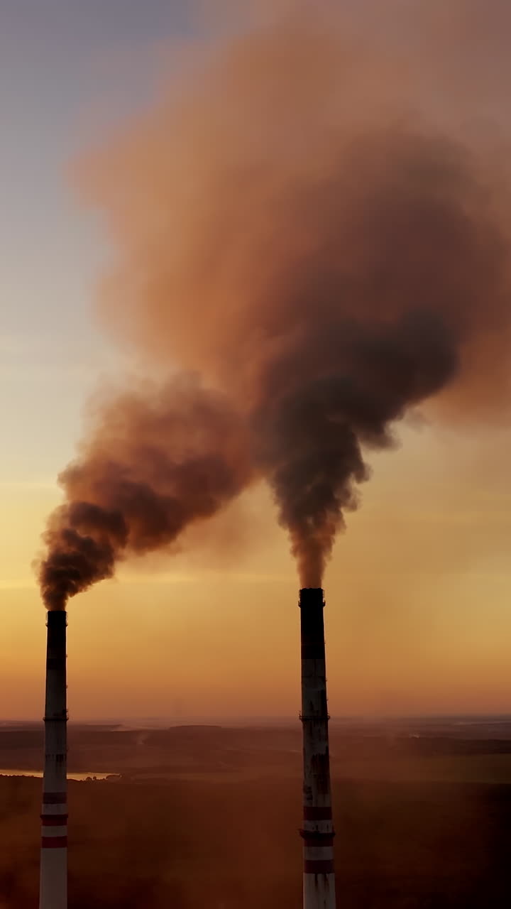 Pollution of the environment. Toxic smoke goes from industrial pipes of the factory at a beautiful sunset. Ecological disaster. Vertical video