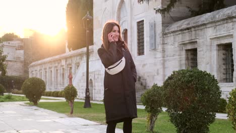 beautiful woman in a black coat writes sms, in a historical park, sunset