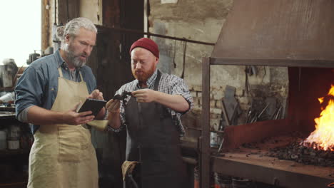 two blacksmiths using tablet while working in smithy