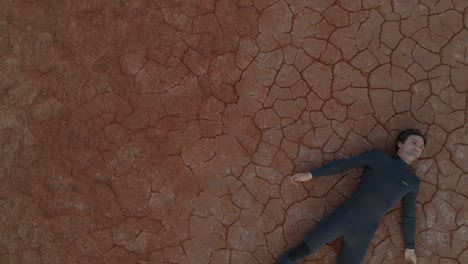 Drone-clip-of-male-model-wearing-wetsuit-lying-on-cracked-desert-ground