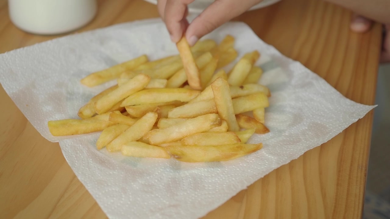 Hand Picking Up a Golden French Fry from a Pile