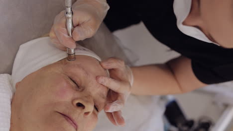 Beautician-makes-senior-woman-vacuum-cleaning-facial-microdermabrasion-diamond-peeling-procedure