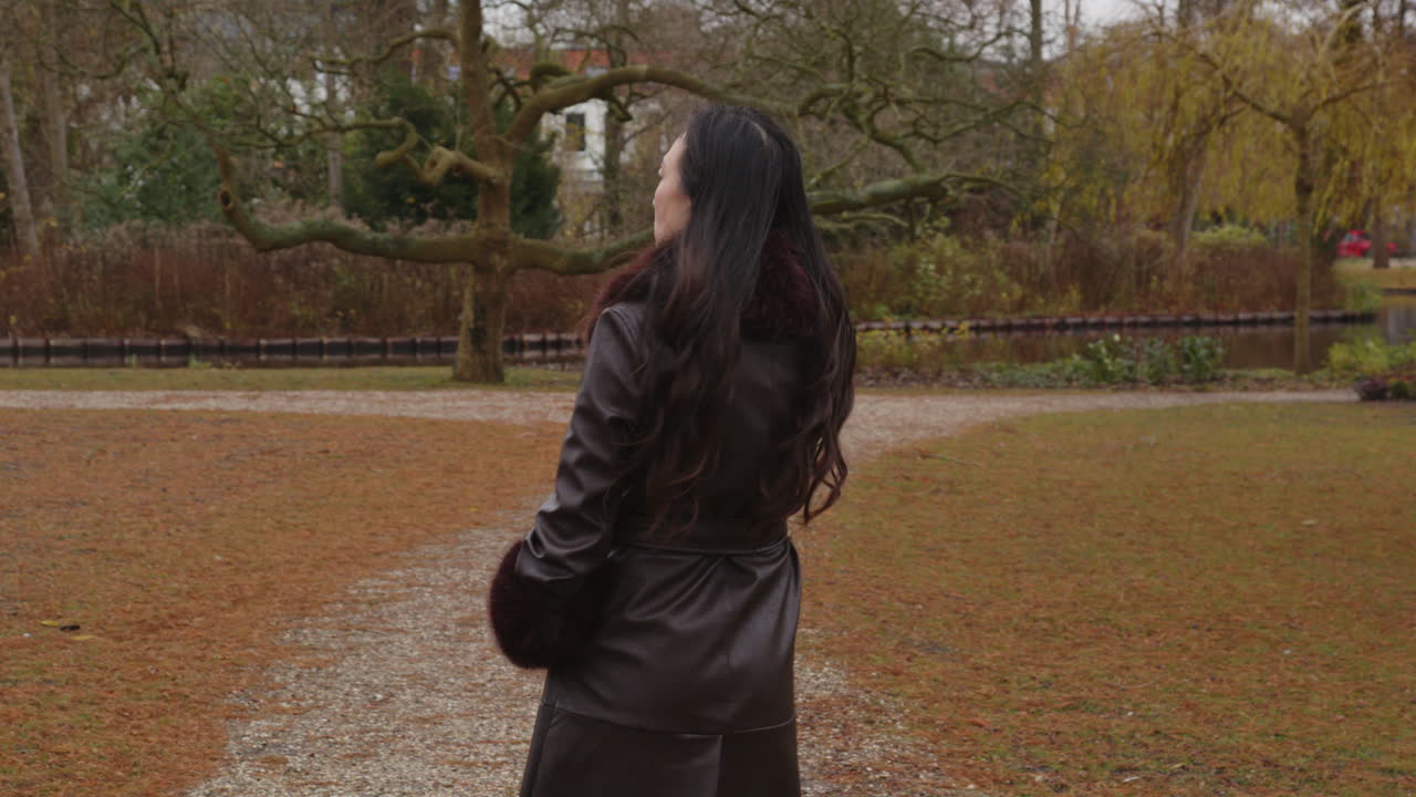 Una donna asiatica sconvolta cammina in un parco mentre telefona a qualcuno con il suo cellulare