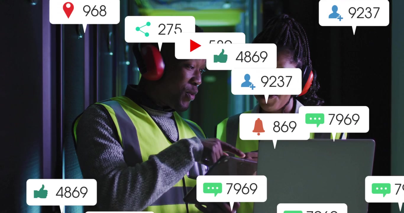 Male tech tapping tablet, female tech checking laptop in data center, managing rising alert badges