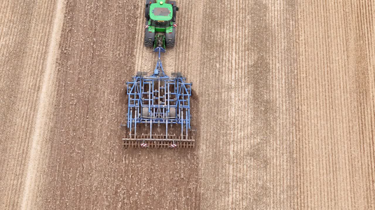 Aerial top down tracking follows tractor pulling mechanism on farmland in Etchilhampton, UK, showcasing post-harvest landscape with visible tractor marks