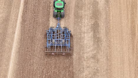 aerial top down tracking follows tractor pulling mechanism on farmland in etchilhampton, uk, showcasing post-harvest landscape with visible tractor marks