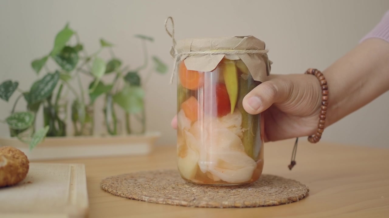Hand hebt ein Glas hausgemachtes eingelegtes Gemüse von einem Holztisch.