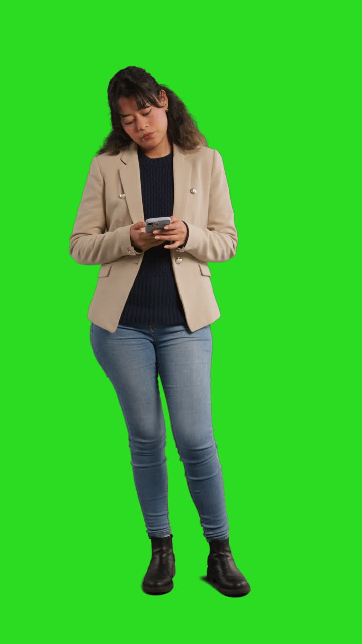 video studio verticale di una donna d'affari che usa il telefono cellulare per inviare messaggi o navigare online in piedi contro lo schermo verde 1