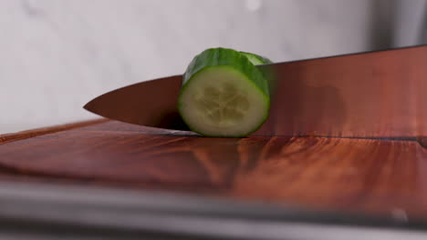Close-up-of-Male-chef-dramatically-and-aggressively-chops-a-green-cucumber-in-slow-motion,-ninja-style-on-a-wooden-chopping-board