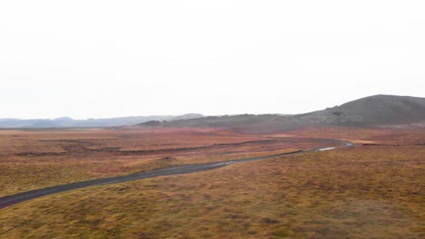 Wet-gravel-road-with-puddles-in-foggy-autumn-heath-landscape,-Iceland