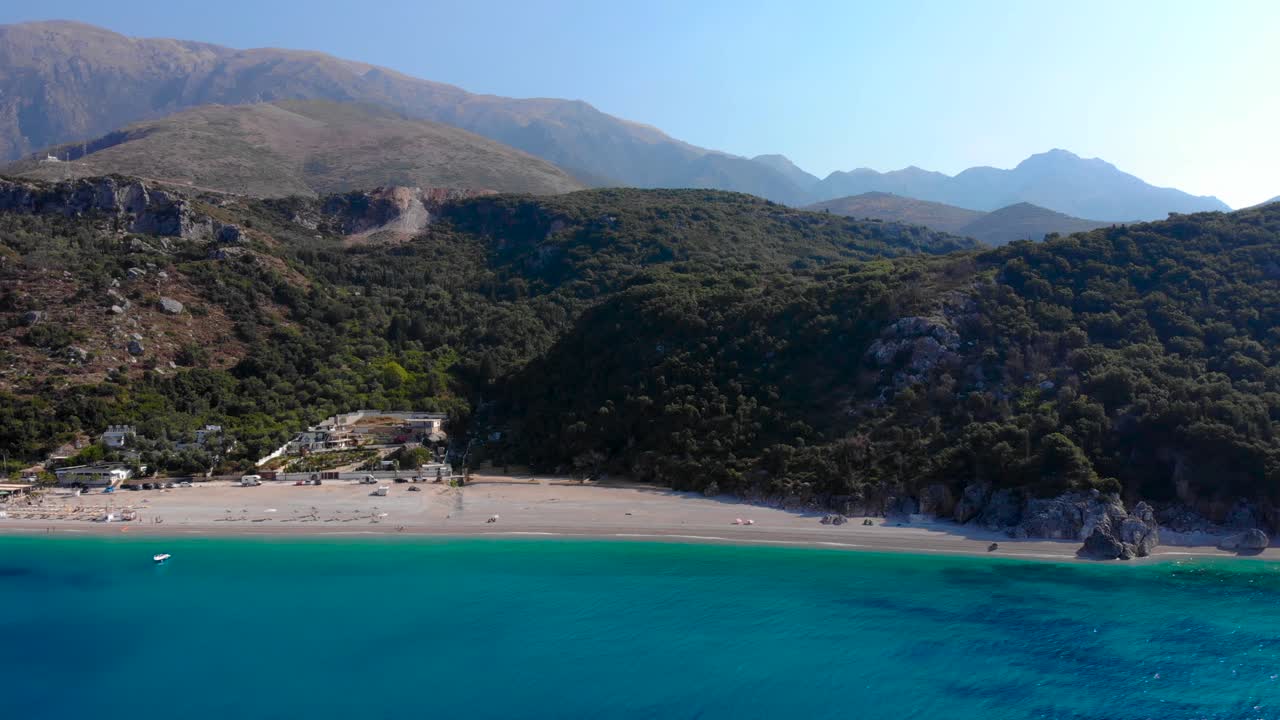 Beautiful sunrise over beach surrounded by green hills and blue azure Ionian sea in Albania
