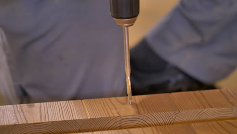 wood worker drills a hole with paddle bit attached to hand drill in thermo pine material