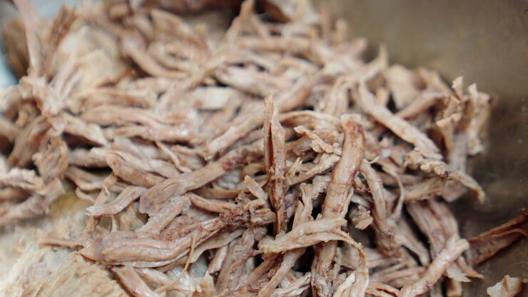 Manzo sfilacciato, cotto lentamente e tenero, in preparazione per un pasto saporito. Focus sulla consistenza e sulla preparazione culinaria