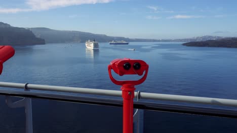 red binoculars at lookout point in santorini greece with cruise ships docked off shore, static