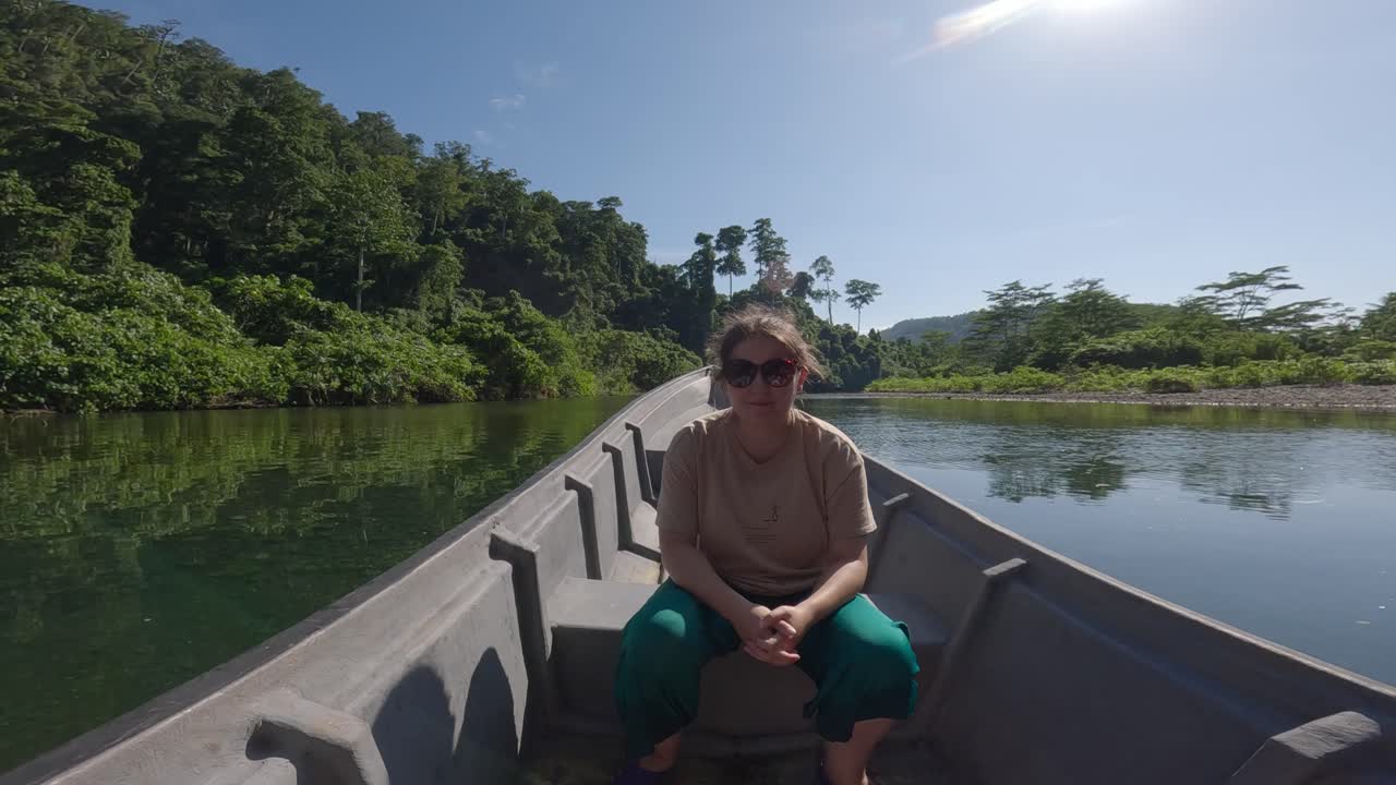 Donna seduta sulla prua di una barca naviga lungo il famoso fiume blu Kali Biru in Indonesia, circondata da una vegetazione lussureggiante.