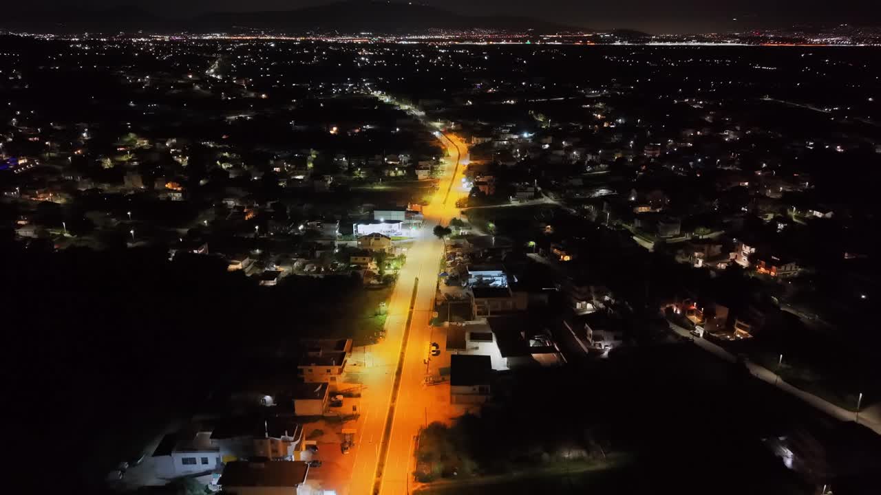 Sopra Porto Rafti nell'Attica Orientale, verso le 23:00, il drone segue con precisione il centro di una strada ben illuminata. Calde luci stradali dorate creano pozze luminose sull'asfalto, dominando il fra