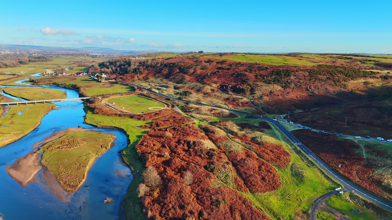 Slingerende rivier door kustheuvels met een weg en een parkeerplaats. Luchtfoto van een rivierbocht naast een weg, parkeerterrein en bruine heuvelvegetatie.