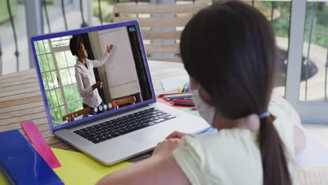 Kaukasisches-Mädchen-Mit-Gesichtsmaske-Führt-Zu-Hause-Einen-Videoanruf-Mit-Einer-Lehrerin-Auf-Einem-Laptop