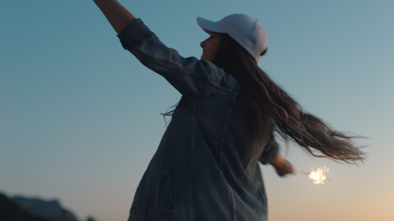 10대 소녀가 해질녘 해변에서 폭죽과 함께 춤을 추며 새해 전야를 축하하며 자유를 즐기는 불꽃놀이와 함께 독립 기념일을 축하하며 즐거운 시간을 보내고 있습니다.