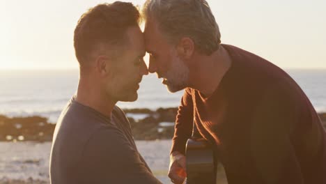 happy caucasian gay male couple sitting on car playing guitar and kissing at the beach