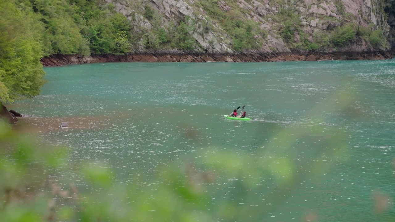 Due persone in kayak attraverso le acque turchesi del Lago Dajes, Slovenia, circondate da rive boscose e colline rocciose. Vista statica