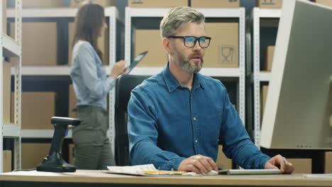 Gray-Haired-Man-In-Glasses-Working-At-Computer-Screen-In-Postal-Delivery-Store-And-Typing-On-Keyboard