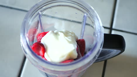 Pouring-yogurt-frozen-blueberries-and-strawberries-into-blender-to-make-smoothie-or-fitness-shake