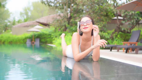 A-young-woman-in-a-bathing-suit-fresh-from-swimming-lies-on-her-stomach-along-the-edge-of-the-pool-while-playfully-kicking-her-feet