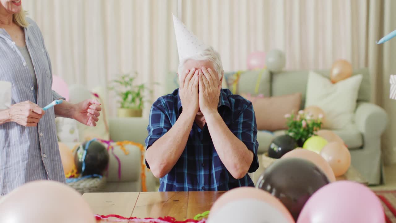 고령 백인 남자가 다양한 고령 친구들과 함께 집에서 생일 파티를 열고 있습니다.