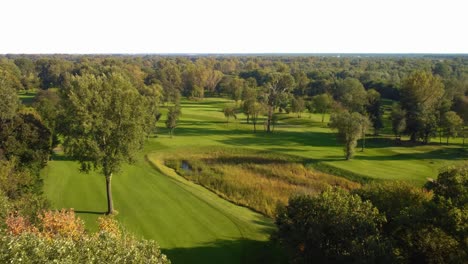 aerial backwards drone shot over a golf course, trees with horizon during sunny summer day