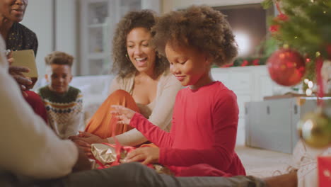 Familia-Multigeneracional-Intercambiando-Y-Abriendo-Regalos-Alrededor-Del-árbol-De-Navidad-En-Casa