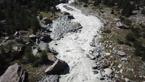 drone aerial view of a muddy river in the swiss alps, rocky mountain valley, strong current and waves