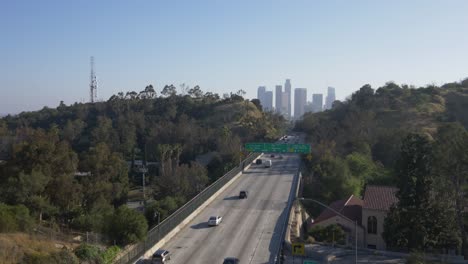drone view of a scenic highway winding through hillside greenery into downtown los angeles. a red-tiled landmark anchors the frame, blending natural contours with urban skyline energy