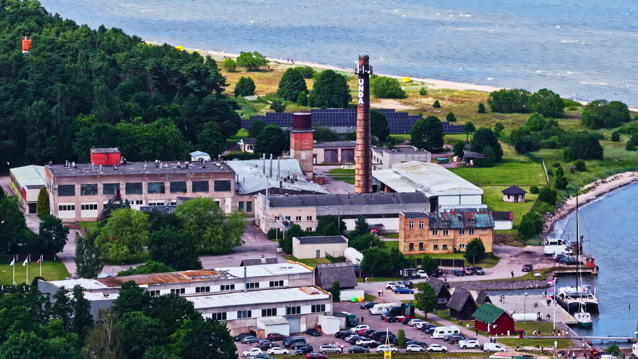 Aerial of Engure’s coastal factory and smoke stack near water on a clear sunny day