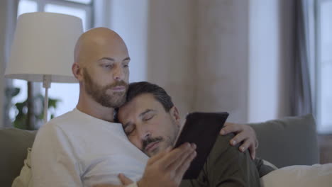 man looking at tablet screen while lying in bed with lover