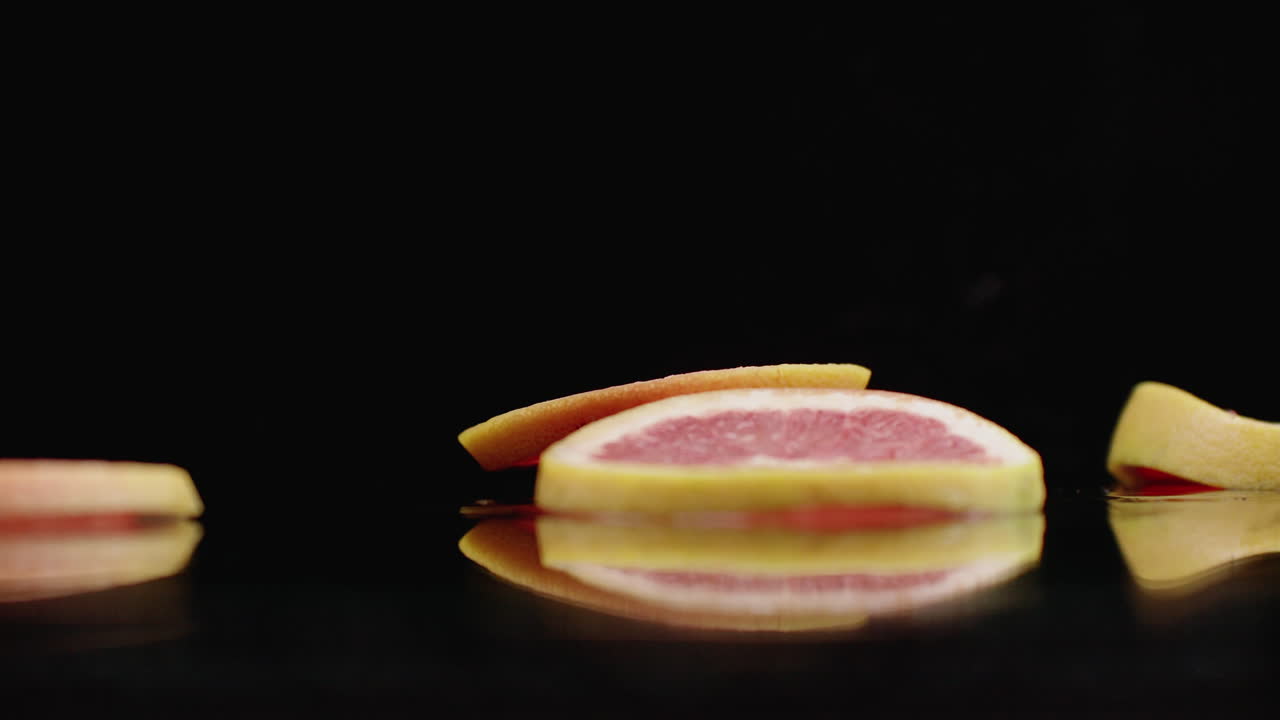 anillos de pomelo en rodajas que caen con salpicaduras de agua en el vaso sobre un fondo oscuro. frutas cítricas jugosos.