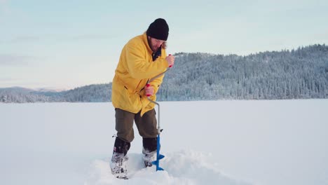 chico noruego está perforando con barrena de hielo en un lago congelado