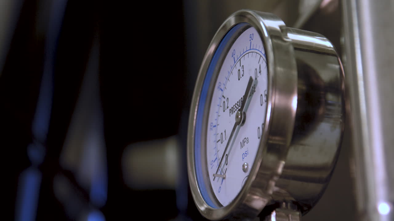 Closeup shot of pressure gauge mounted on a stainless steel fermentation tank in a brewery, ending in an out-of-focus view