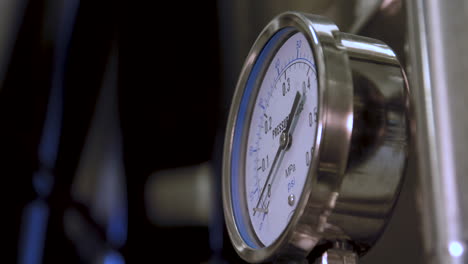 closeup shot of pressure gauge mounted on a stainless steel fermentation tank in a brewery, ending in an out-of-focus view