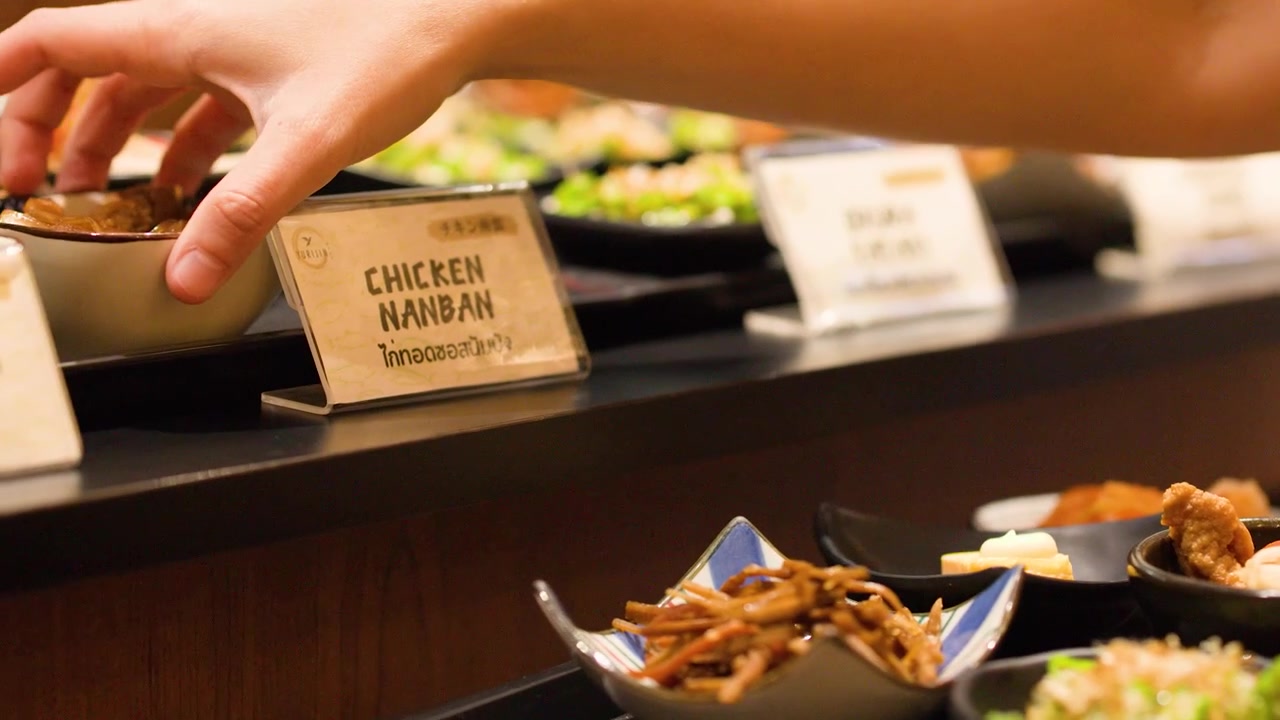 Käsi kurkottaa kohti kulhoa chicken nanbania japanilaisessa buffetravintolassa