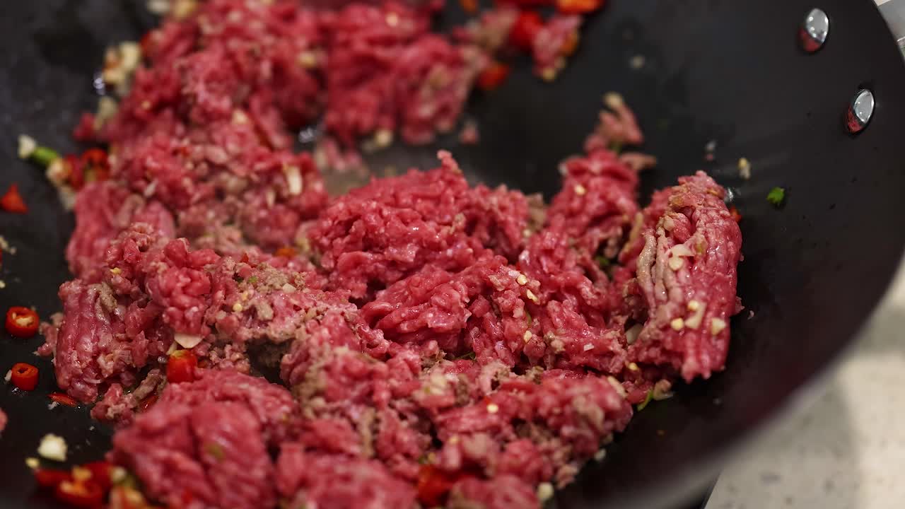 Ground beef is stir-fried with spices in a wok, highlighting vibrant colors and dynamic cooking action