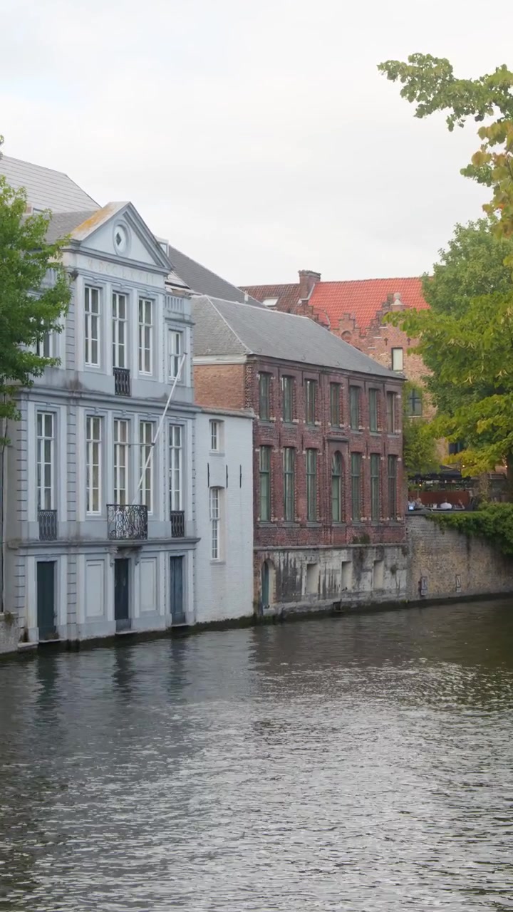 Ripresa stabile diurna del canale di Bruges, edifici storici lungo il fiume, alberi autunnali e delicati riflessi