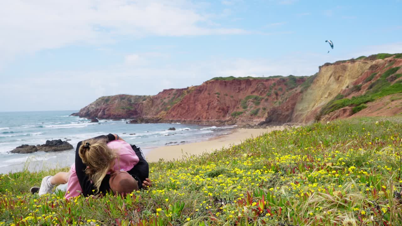 Woman Lies On Top Of Her Boyfriend Lying On The Flower Field By The Beach In Algarve, Portugal. - static shot